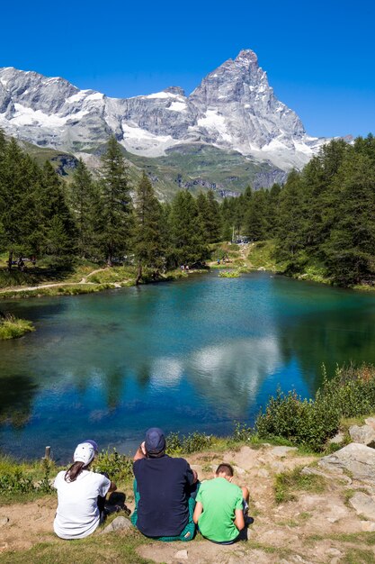 Colpo verticale di un popolo seduto vicino a uno stagno circondato da alberi con una montagna in lontananza