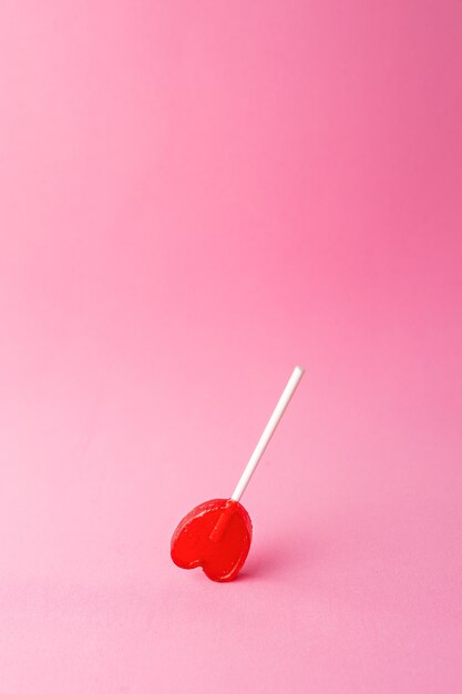 Colpo verticale di un unico lecca-lecca a forma di cuore su uno sfondo rosa