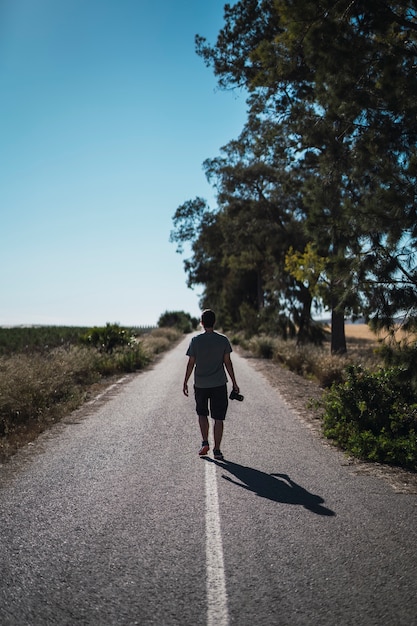 Colpo verticale di un uomo con una macchina fotografica che cammina nel mezzo di una strada deserta con alberi sul lato