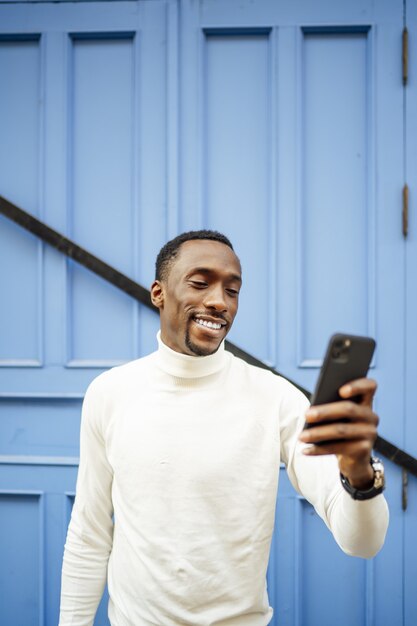 Colpo verticale di un uomo di colore che indossa un dolcevita guardando il suo telefono