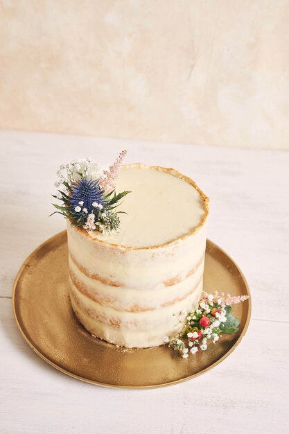 Colpo verticale di una bella e deliziosa torta con fiori e bordi dorati su sfondo bianco