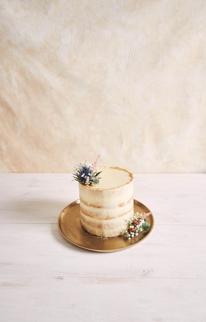 Colpo verticale di una bella e deliziosa torta con fiori e bordi dorati su sfondo bianco