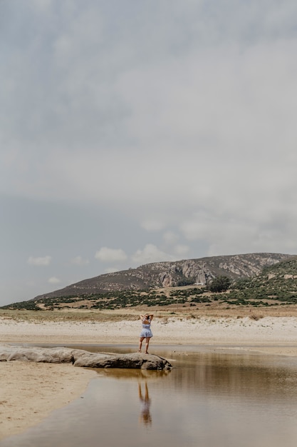 Colpo verticale di una donna in piedi sulla riva con le montagne sullo sfondo