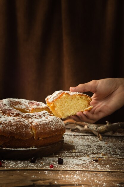 Colpo verticale di una mano che prende un pezzo di un delizioso pan di spagna con zucchero a velo