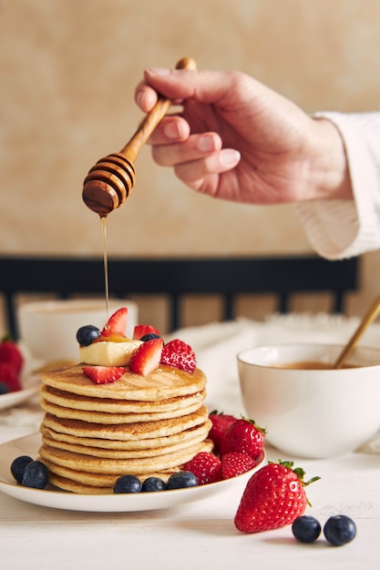 Colpo verticale di una persona che mette lo sciroppo su frittelle di tofu vegano con frutta