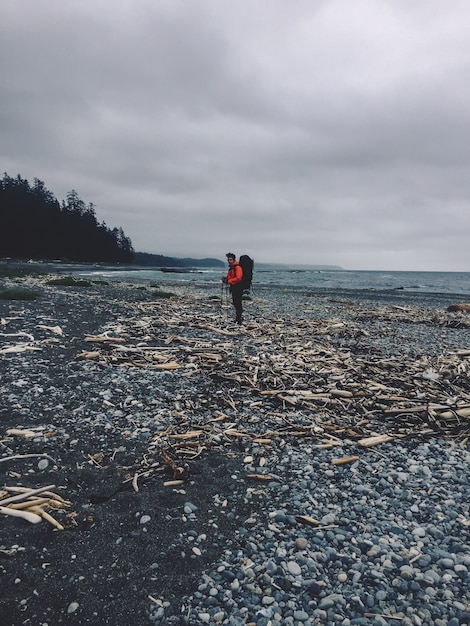 Colpo verticale di una persona in piedi su una spiaggia rocciosa vicino all'oceano