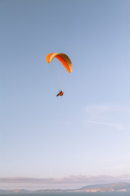 Colpo verticale di una persona sola che paracaduta giù sotto il bello cielo blu