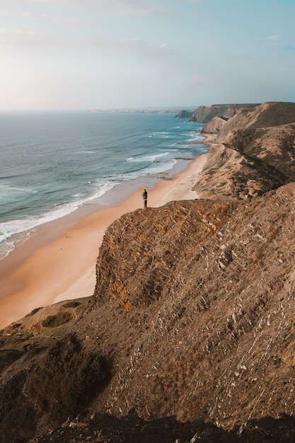 Colpo verticale di una persona su una scogliera guardando il bellissimo oceano in Algarve, Portogallo