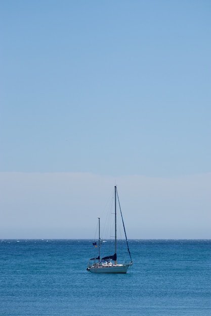 Colpo verticale di una piccola barca che naviga nell'oceano con un cielo blu chiaro