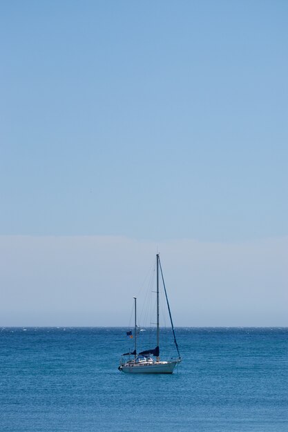 Colpo verticale di una piccola barca che naviga nell'oceano con un cielo blu chiaro
