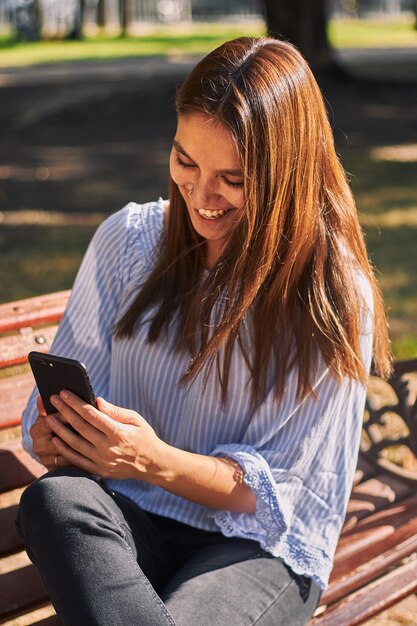 Colpo verticale di una ragazza seduta sulla panchina e guardando il suo telefono