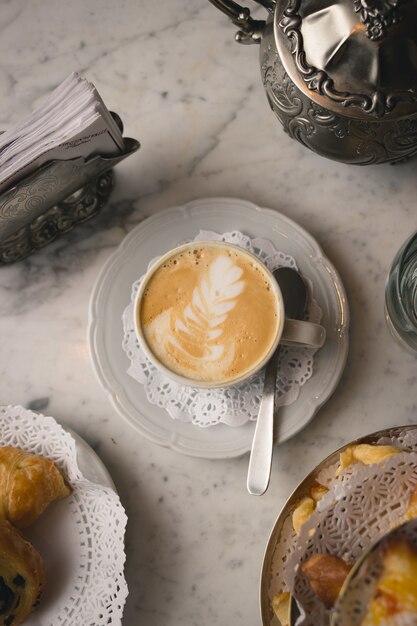 Colpo verticale di una tazza di cappuccino sul tavolo di marmo con dessert