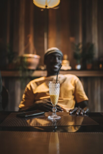 Colpo verticale di una tazza di frullato su un tavolo davanti a un maschio afroamericano