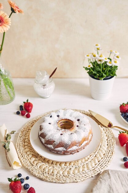 Colpo verticale di una torta ad anello con frutta e polvere su un tavolo bianco con sfondo bianco