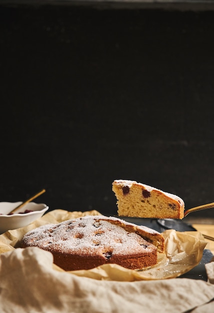 Colpo verticale di una torta di ciliegie con zucchero in polvere e ingredienti sul lato su sfondo nero