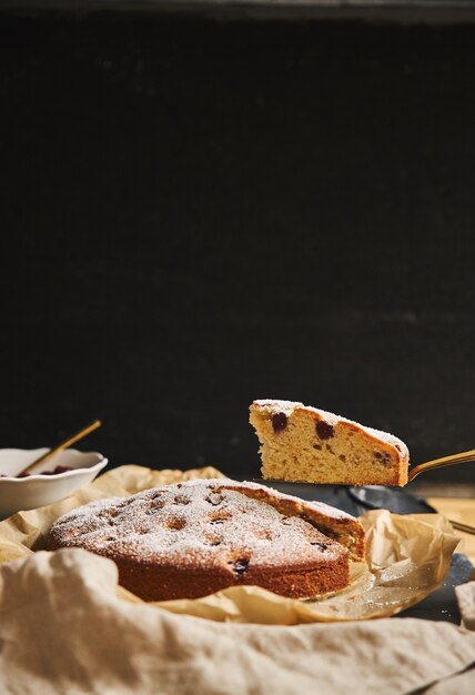 Colpo verticale di una torta di ciliegie con zucchero in polvere e ingredienti sul lato su sfondo nero