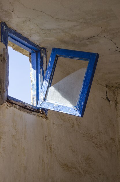 Colpo verticale di una vecchia finestra blu rustica che sta per rompersi e cadere nella stanza fatiscente