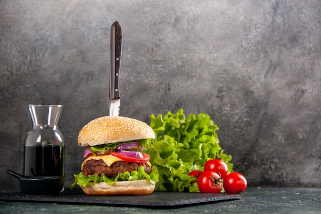 Coltello in delizioso panino di carne e pepe verde su salsa di vassoio nero pomodori con gambo sul lato destro su superficie grigia