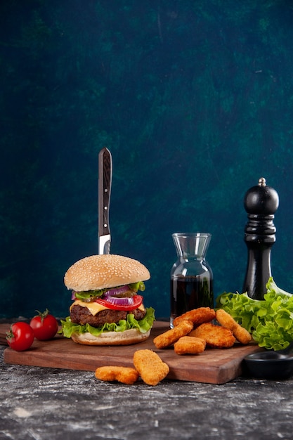 Coltello in sandwich di carne e pepite di pollo pomodori con pepe a gambo su tavola di legno salsa ketchup su superficie blu scuro