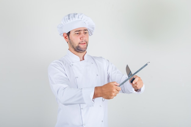 Coltello per affilare chef maschio in uniforme bianca e guardando occupato
