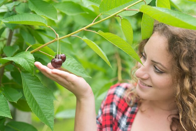 Coltivatore della bella donna che tiene la frutta della ciliegia nel frutteto verde