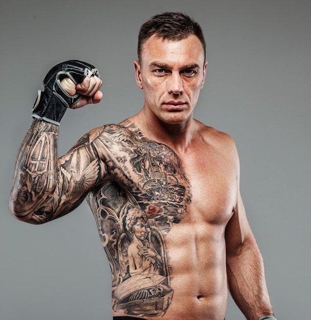 Combattente tatuato muscolare su sfondo grigio. Studio girato