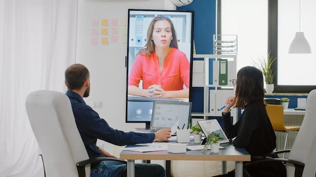 Compagni di lavoro che utilizzano la videochiamata in televisione per conversare con una donna sul progetto aziendale. Colleghi che parlano con il manager durante una conferenza online per la strategia di briefing sulla presentazione