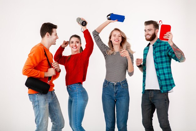 Compagnia di giovani hipster di amici che si divertono insieme sorridendo ascoltando musica su altoparlanti wireless ballando ridendo sfondo bianco studio isolato in abito colorato ed elegante