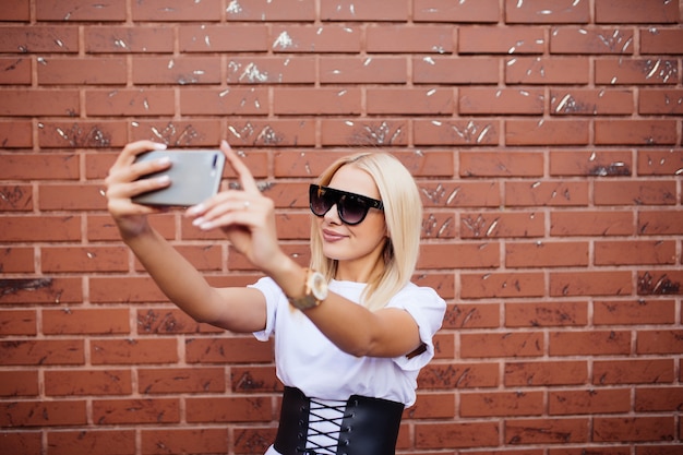 Composito Digitale della donna millenaria prendendo selfie contro il muro di mattoni rossi