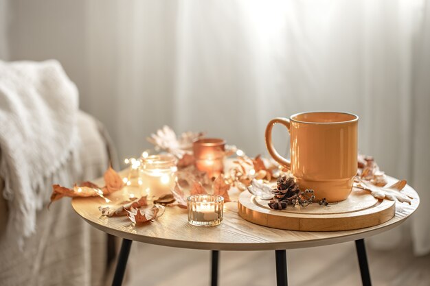 Composizione accogliente con una tazza, candele e foglie autunnali all'interno.