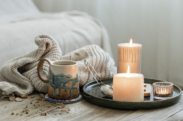 Composizione accogliente con una tazza in ceramica, candele e un elemento a maglia su uno sfondo sfocato.