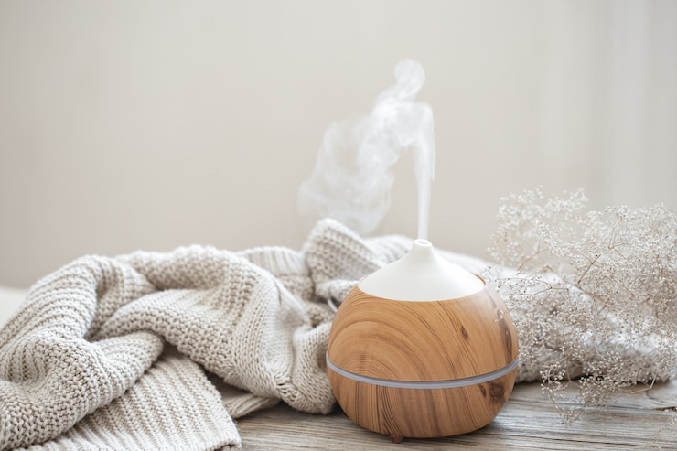 Foto gratuito composizione aromatica con un moderno diffusore di oli aromatici su una superficie di legno con un elemento in maglia e un rametto di fiori secchi.