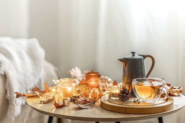 Composizione autunnale domestica con tè, foglie secche e candele accese su sfondo sfocato, spazio copia.