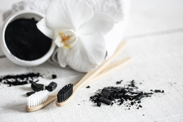 Composizione con spazzolini da denti naturali in legno, polvere sbiancante per denti neri e spazio per la copia di fiori di orchidea.