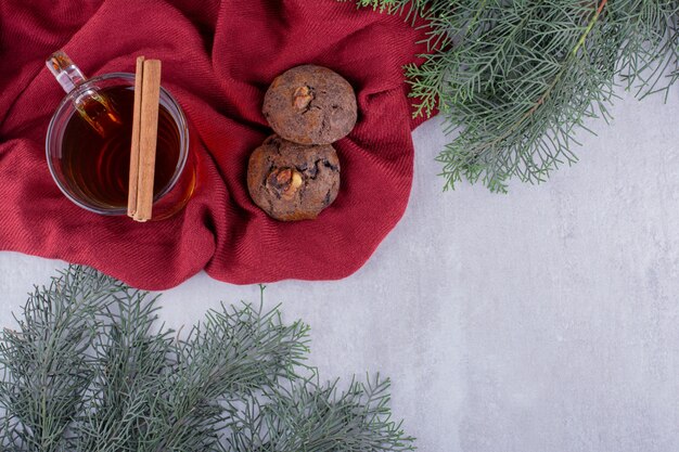 Composizione di biscotti, stecca di cannella e una tazza di tè su sfondo bianco.