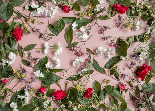 Composizione floreale con diversi fiori freschi, foglie e ramoscelli su una superficie rosa