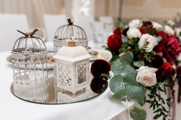 Composizione floreale con rose di eucalipto, bianche e bordeaux sul tavolo e gabbie di metallo su un vassoio a specchio