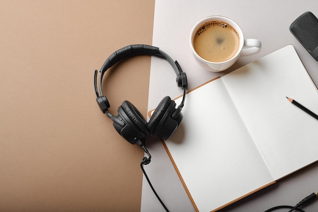 Composizione piatta con microfono per podcast e cuffie da studio nere su sfondo marrone con caffè e laptop che imparano il concetto di formazione online