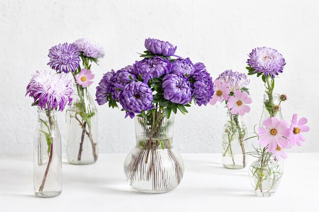 Composizione primaverile con fiori di crisantemo in vasi di vetro su uno sfondo bianco sfocato.