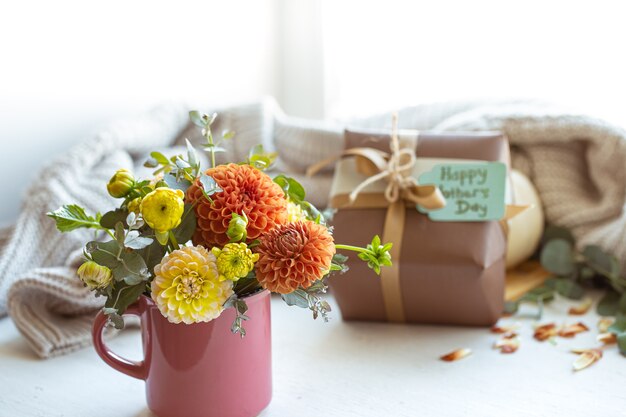 Composizione primaverile per la festa della mamma con regalo, fiori di crisantemo ed elemento a maglia.