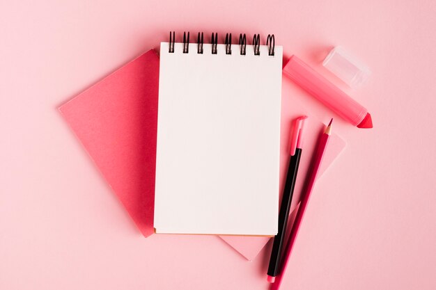 Composizione rosa con blocco note e articoli per ufficio su superficie colorata