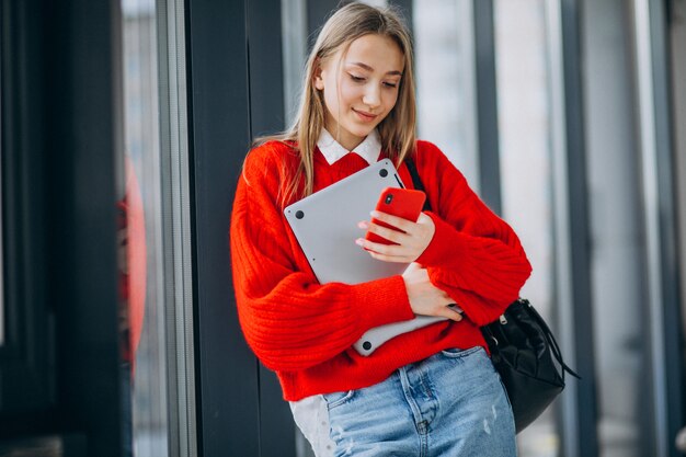 Computer della tenuta della studentessa e parlare al telefono dalla finestra