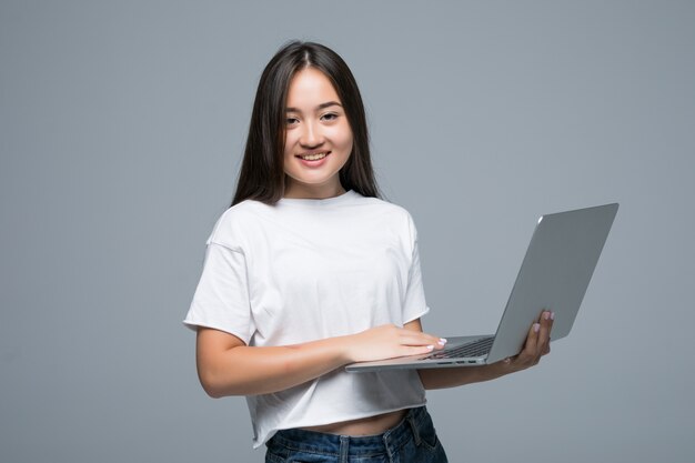 Computer portatile asiatico della tenuta della donna mentre esaminando la macchina fotografica sopra fondo grigio