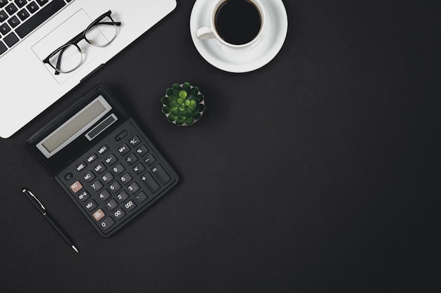 Computer portatile bicchieri tazza di caffè e calcolatrice su sfondo nero vista dall'alto