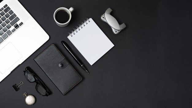 Computer portatile con cancelleria per ufficio e accessori personali con una tazza di tè su sfondo nero