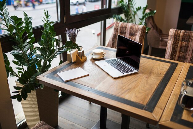 Computer portatile con il blocco note in caffè sul tavolo