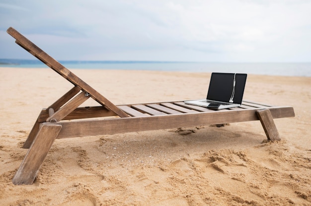 Computer portatile con le cuffie sulla sedia di spiaggia con la sabbia