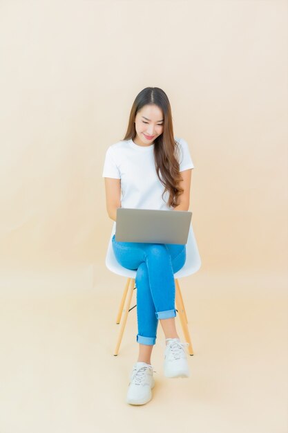 Computer portatile del computer di uso della bella giovane donna asiatica del ritratto sul beige