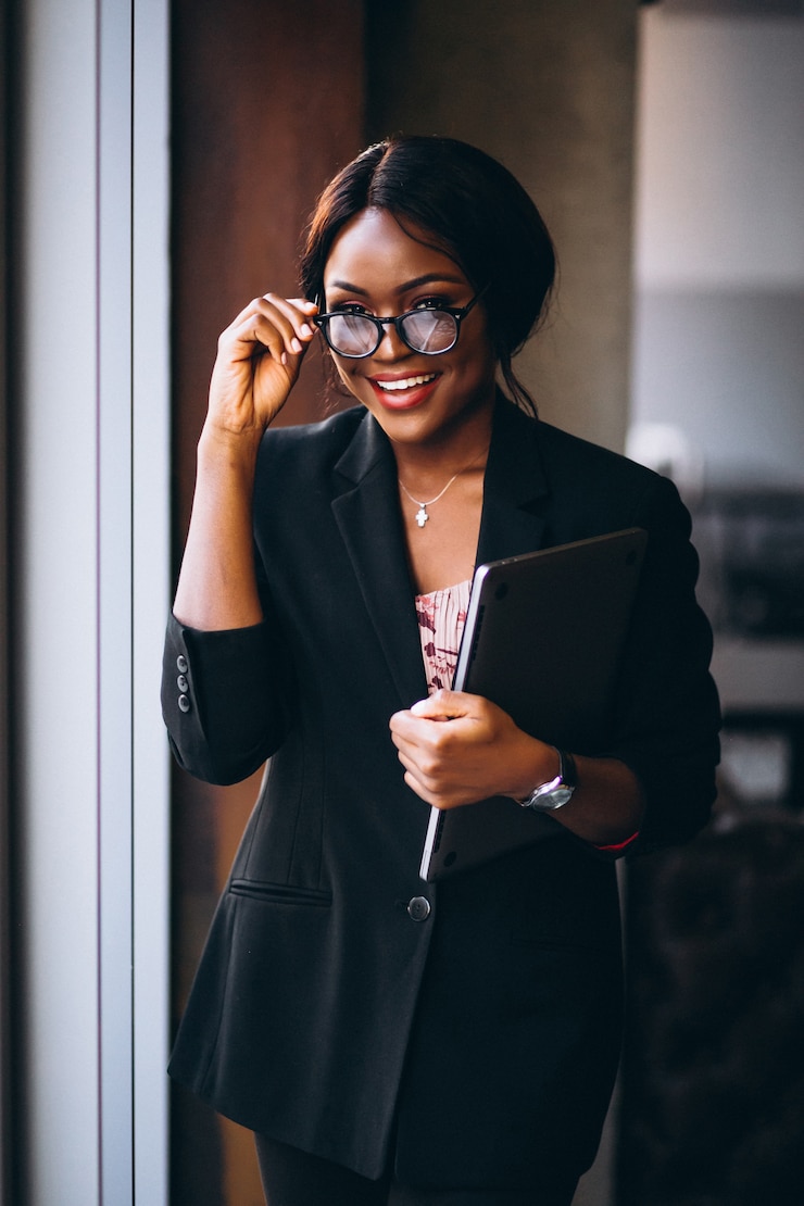 Foto gratuito computer portatile della tenuta della donna di affari dell'afroamericano e condizione vicino alla finestra