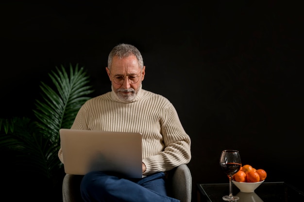 Computer portatile di navigazione dell&#39;uomo anziano vicino a mandarini e vino